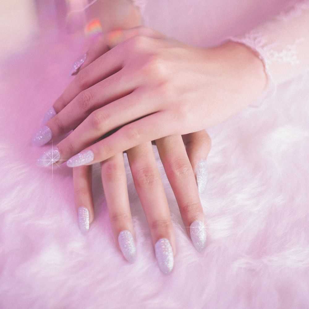 Hand with glittery nails resting on a pink furry surface.