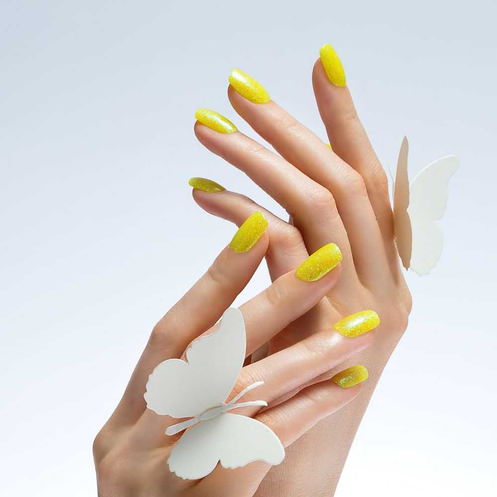Hands with yellow glitter nail polish and a paper butterfly.