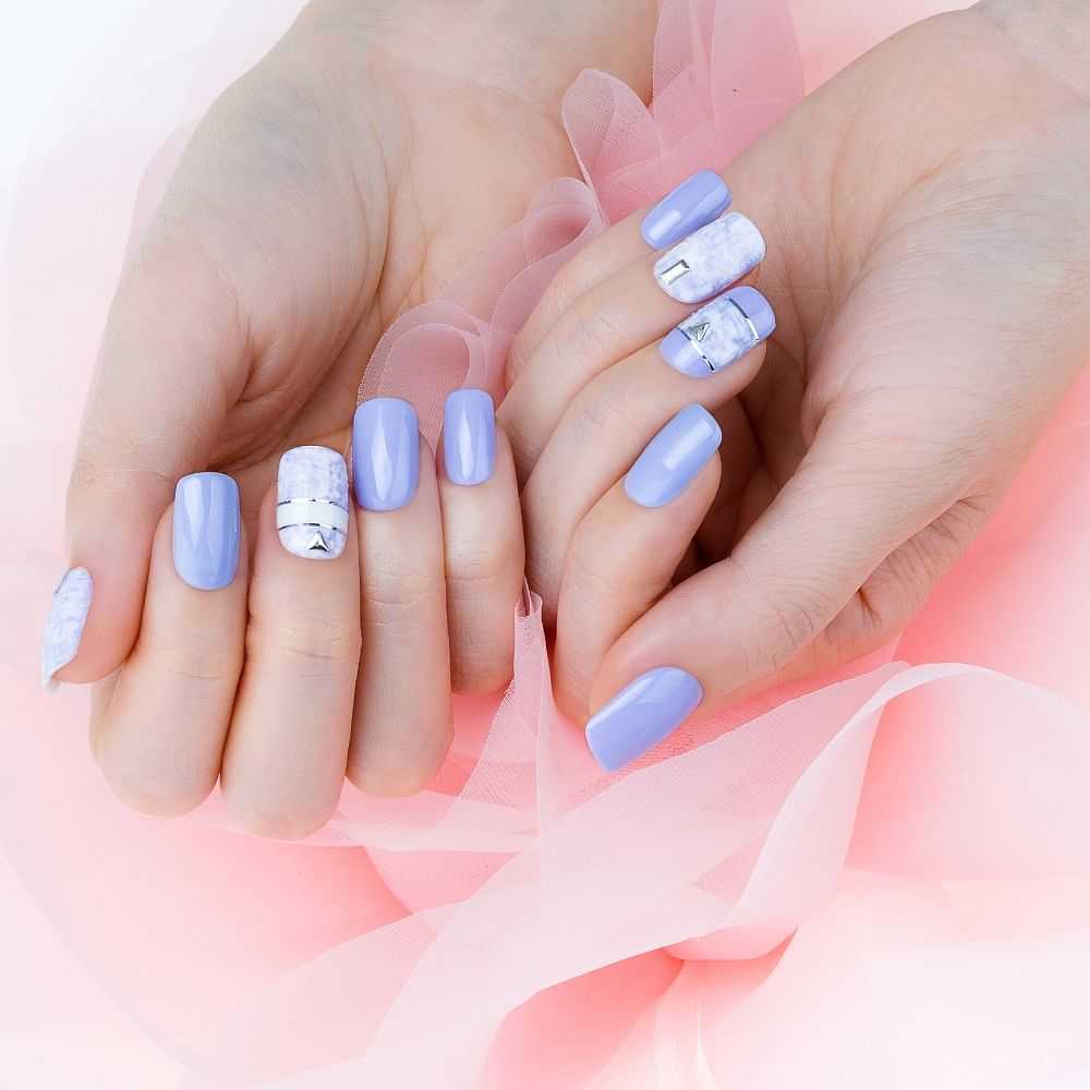 Hands with lilac nail polish and marble design against pink fabric.