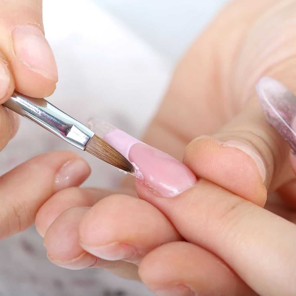 Applying pink polish to fingernail with a brush.