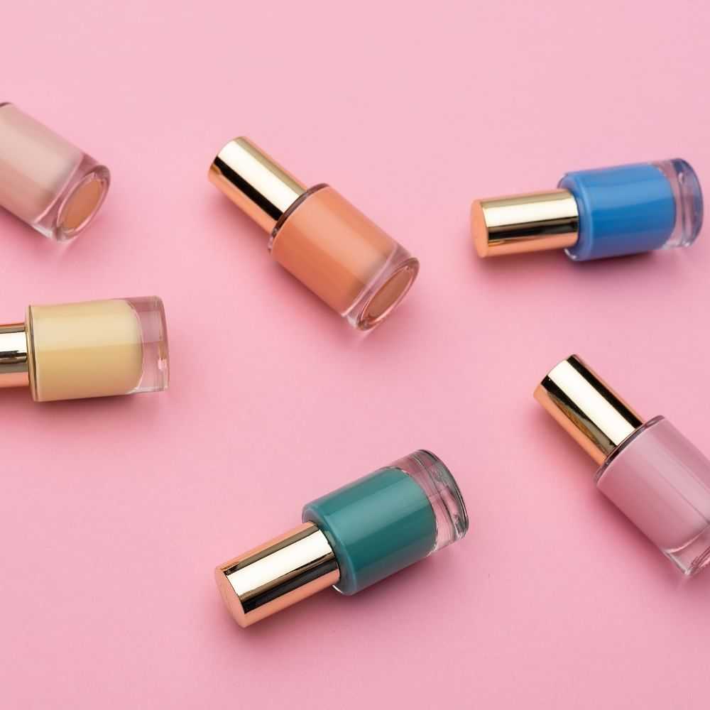 Array of colorful nail polish bottles on a pink background.