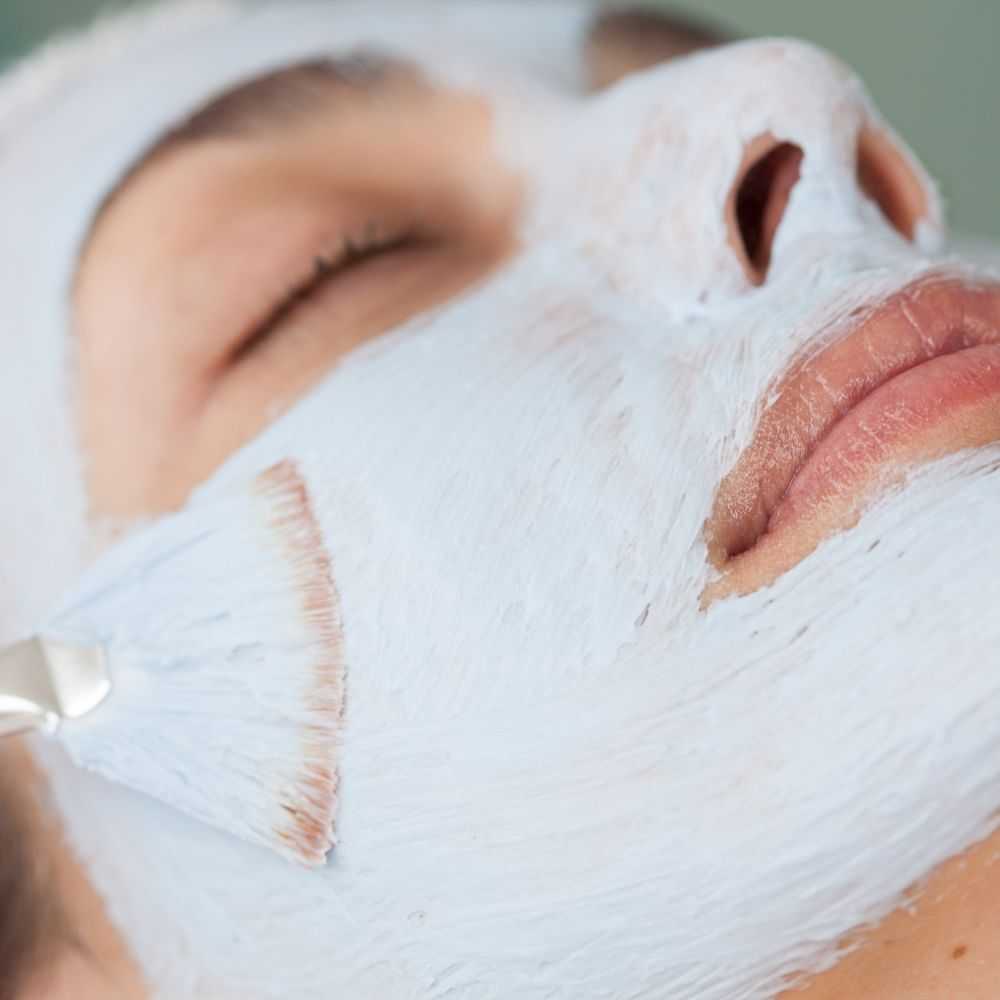 Person receiving a facial mask treatment with a brush.