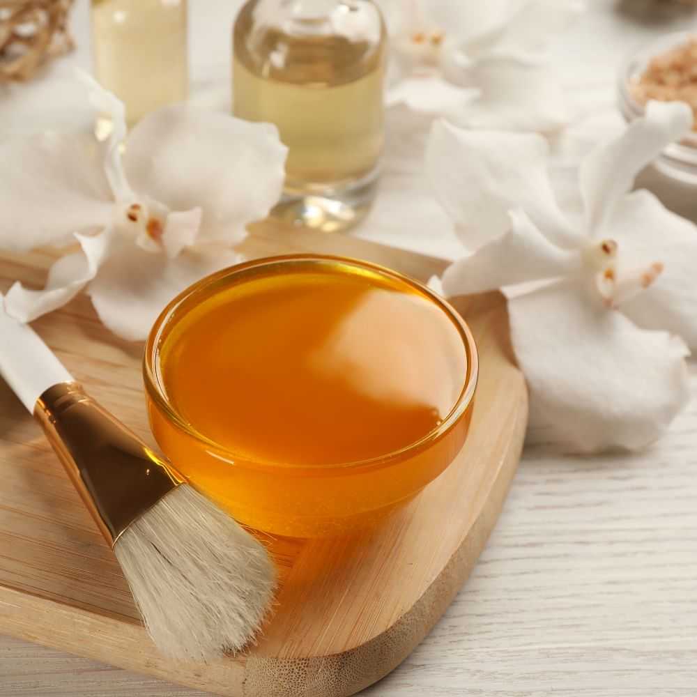 Jar of honey with brush and cotton flowers on a wooden board.