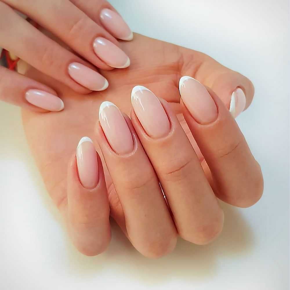 Elegant manicured hands with natural pink nails on a white surface.